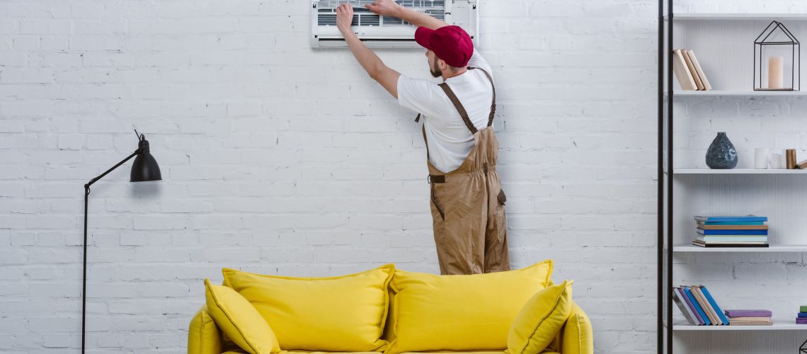 professional repairman changing filter for air conditioner hanging on white brick wall